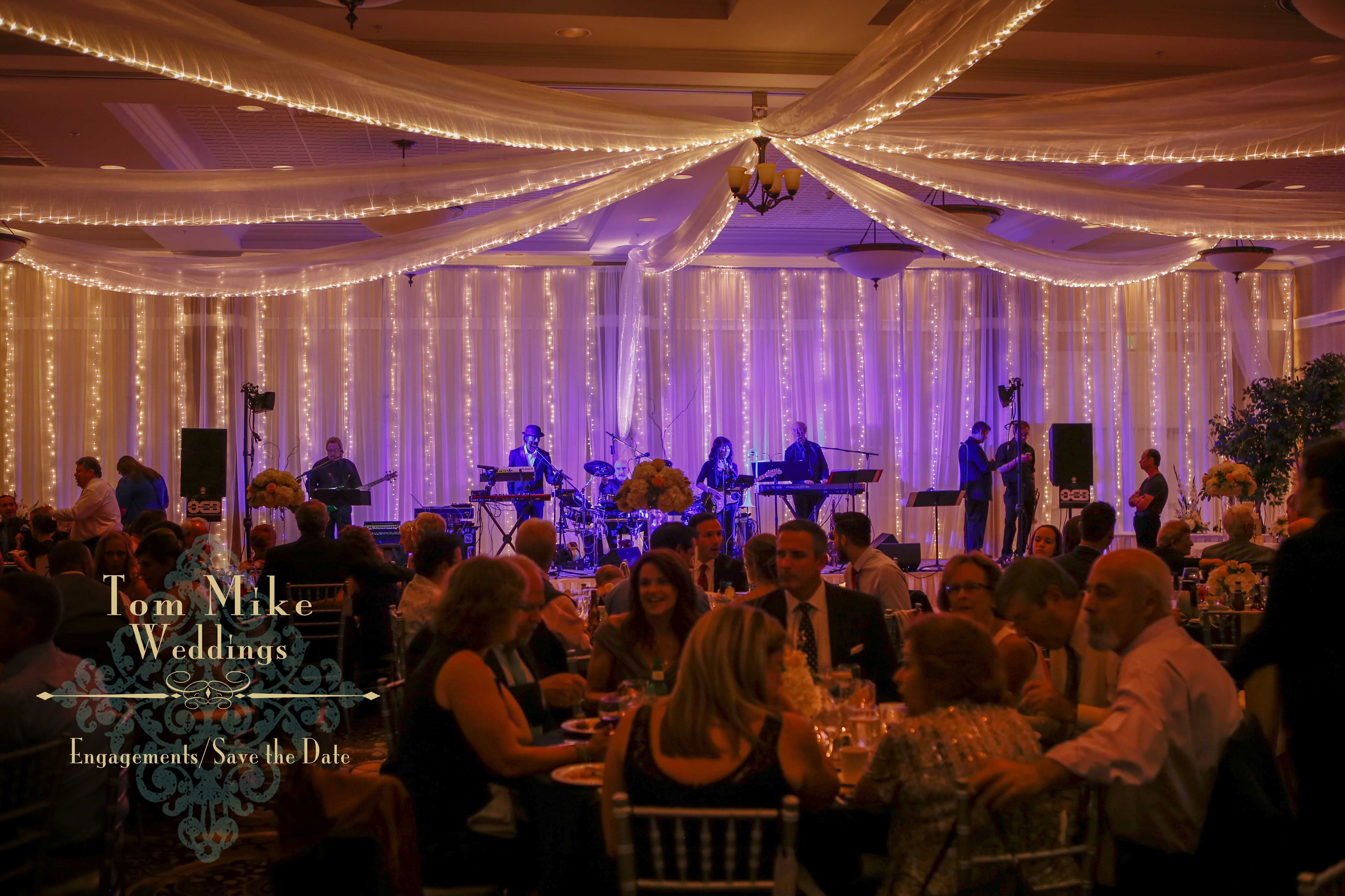 Ballroom with ceiling draping and a band playing in the background while guests dine at their tables